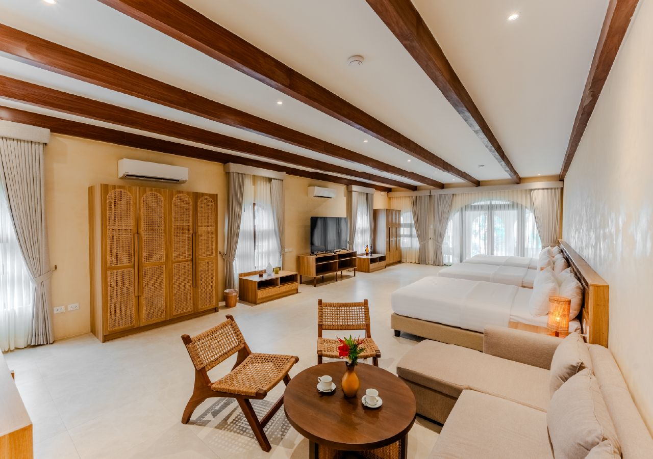 Una habitación de hotel con una cama grande, un sofá, una mesa de comedor, sillas de mimbre y un televisor.