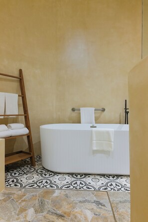 A bathroom with a bathtub, a wooden shelf with towels, and patterned floor tiles.