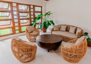 A wicker sofa set with a round coffee table, large windows, and potted plants. - Costa Solana Resort Managed by HII (Pagbilao)