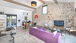 Een moderne woonkamer met een stenen muur, een paarse bank, een eethoek met stoelen, een televisie en een boekenkast.