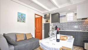 Ein kompakter Wohnbereich mit Sofa, Esstisch, Weingläsern, einer Mikrowelle und einer gefliesten Rückwand.