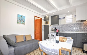 Ein kompakter Wohnbereich mit Sofa, Esstisch, Weingläsern, einer Mikrowelle und einer gefliesten Rückwand.