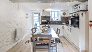 Una cocina moderna con armarios blancos, una mesa de comedor con sillas, una cafetera y un horno.
