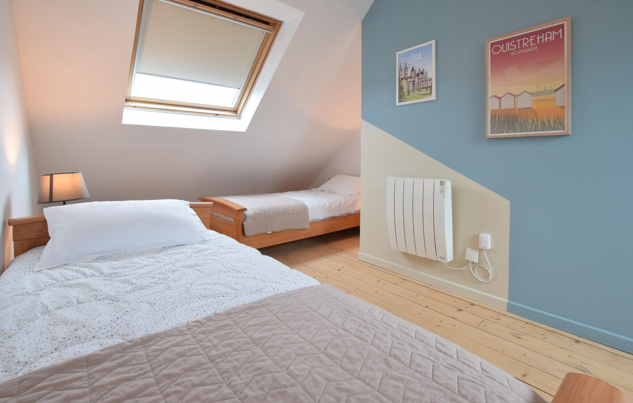 A bedroom with a skylight, a bed with a quilt, a bedside table with a lamp, and a radiator on the wall.