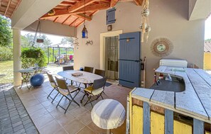 Eine überdachte Terrasse mit einem runden Tisch, Stühlen, einer Tür und einem kleinen Tisch mit Spüle.