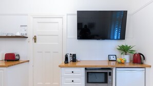 A compact kitchen with a microwave, toaster, and a small refrigerator. A flat-screen TV is mounted above the counter.