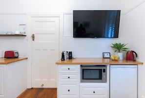 Eine kompakte Küche mit Mikrowelle, Toaster und einem kleinen Kühlschrank. Ein Flachbildfernseher ist über der Arbeitsfläche angebracht.