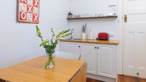 A kitchen with white cabinets, a wooden countertop, a red toaster, and a hanging sign with letters.