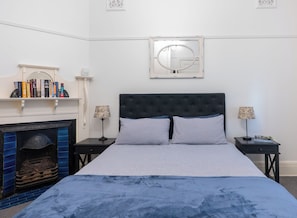 Ein Schlafzimmer mit einem Bett, zwei Nachttischen, einem Kamin und einem an der Wand befestigten Spiegel.