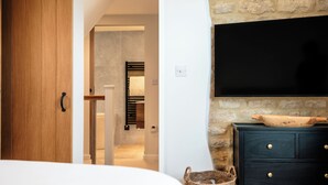Ein Schlafzimmer mit Holztür, einem Bett, einem an einer Steinwand befestigten Fernseher und einer dunklen Kommode mit Schubladen.