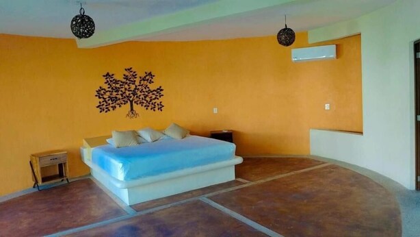 Un dormitorio con cama, mesita de noche, aire acondicionado instalado en la pared y un adhesivo decorativo con forma de árbol.