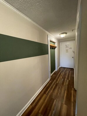 Een gang met een houten vloer, witte muren en een groene streep.