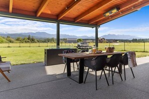 Eine Terrasse im Freien mit Holztisch und -stühlen, einem Grill und Blick auf die Berge.