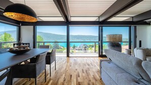 Un interior modern amb zona de menjador, sofà i finestres grans que ofereixen vista a les muntanyes.