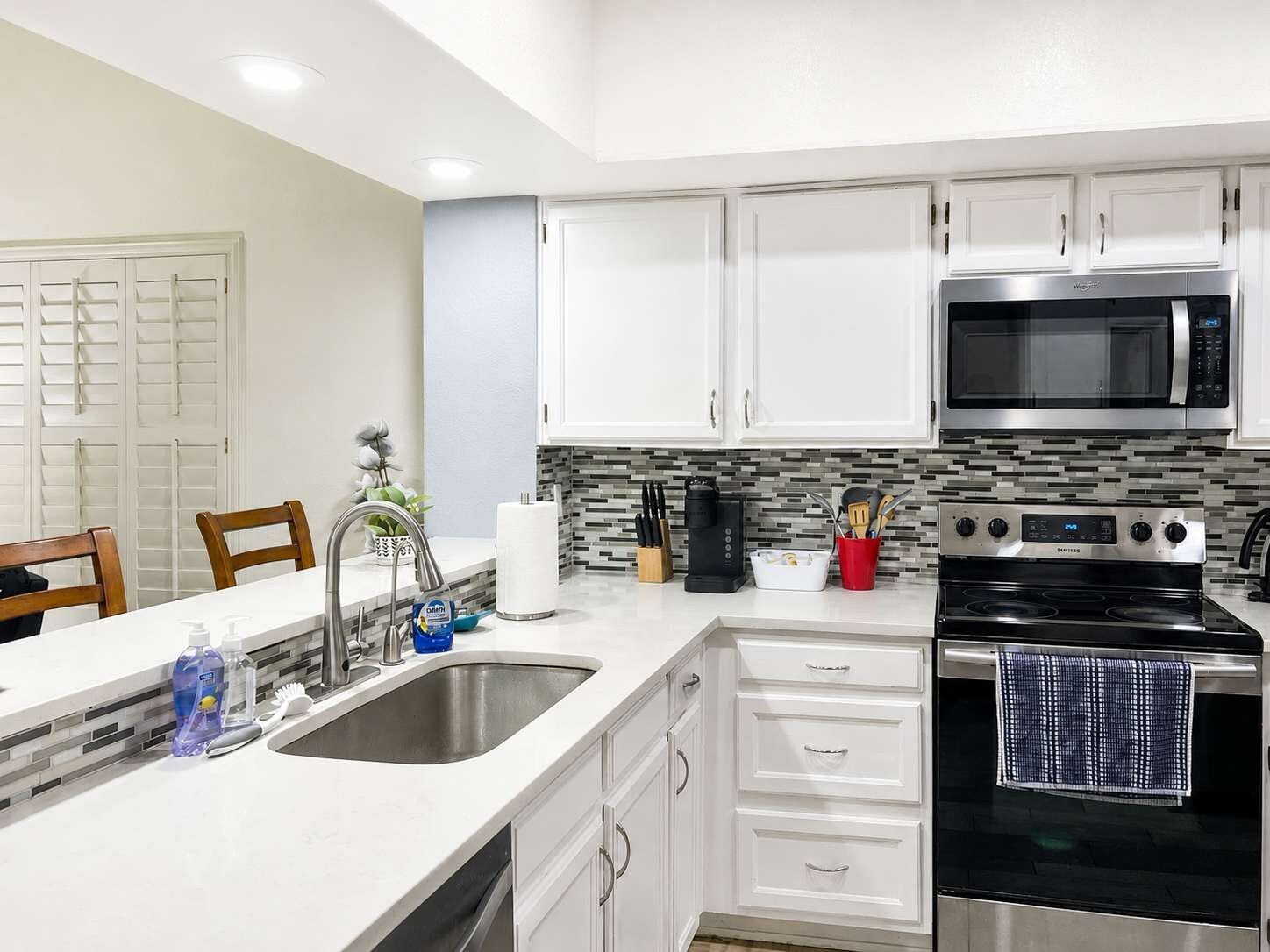 A modern kitchen with white cabinets, a stainless steel microwave, a black stove, and a tiled backsplash.