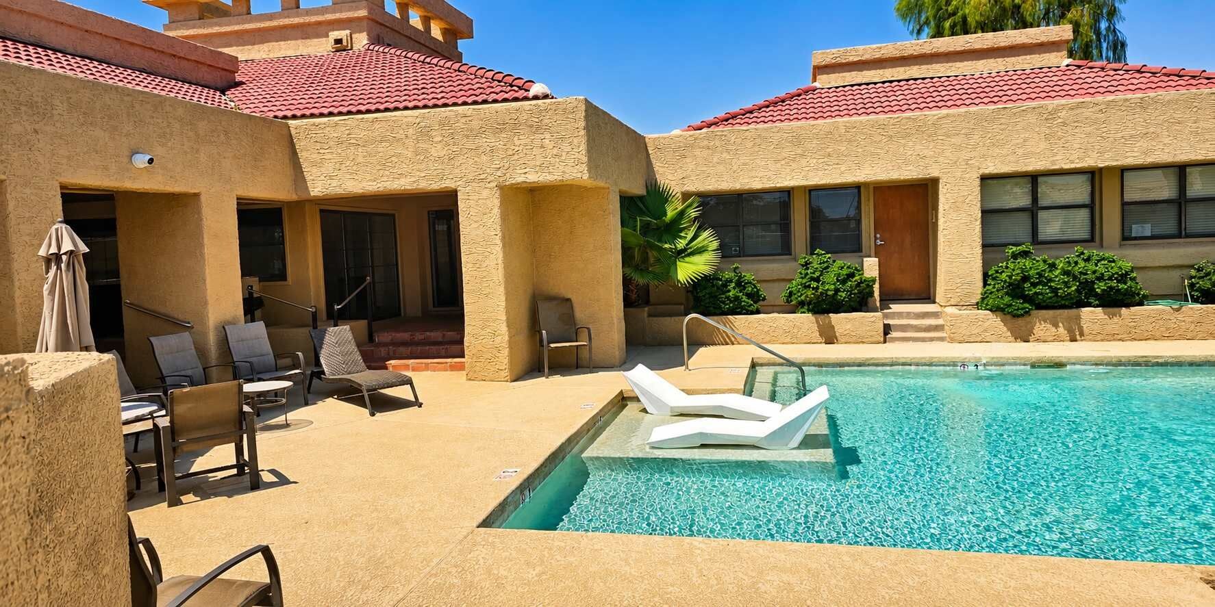 Un área de piscina con sillones de descanso, una piscina cristalina y un edificio con tejado de tejas rojas.