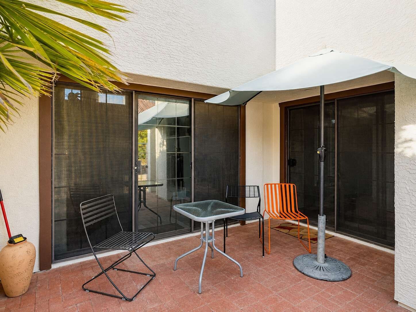 Un patio exterior con una mesa y sillas, un paraguas grande y una planta en maceta.