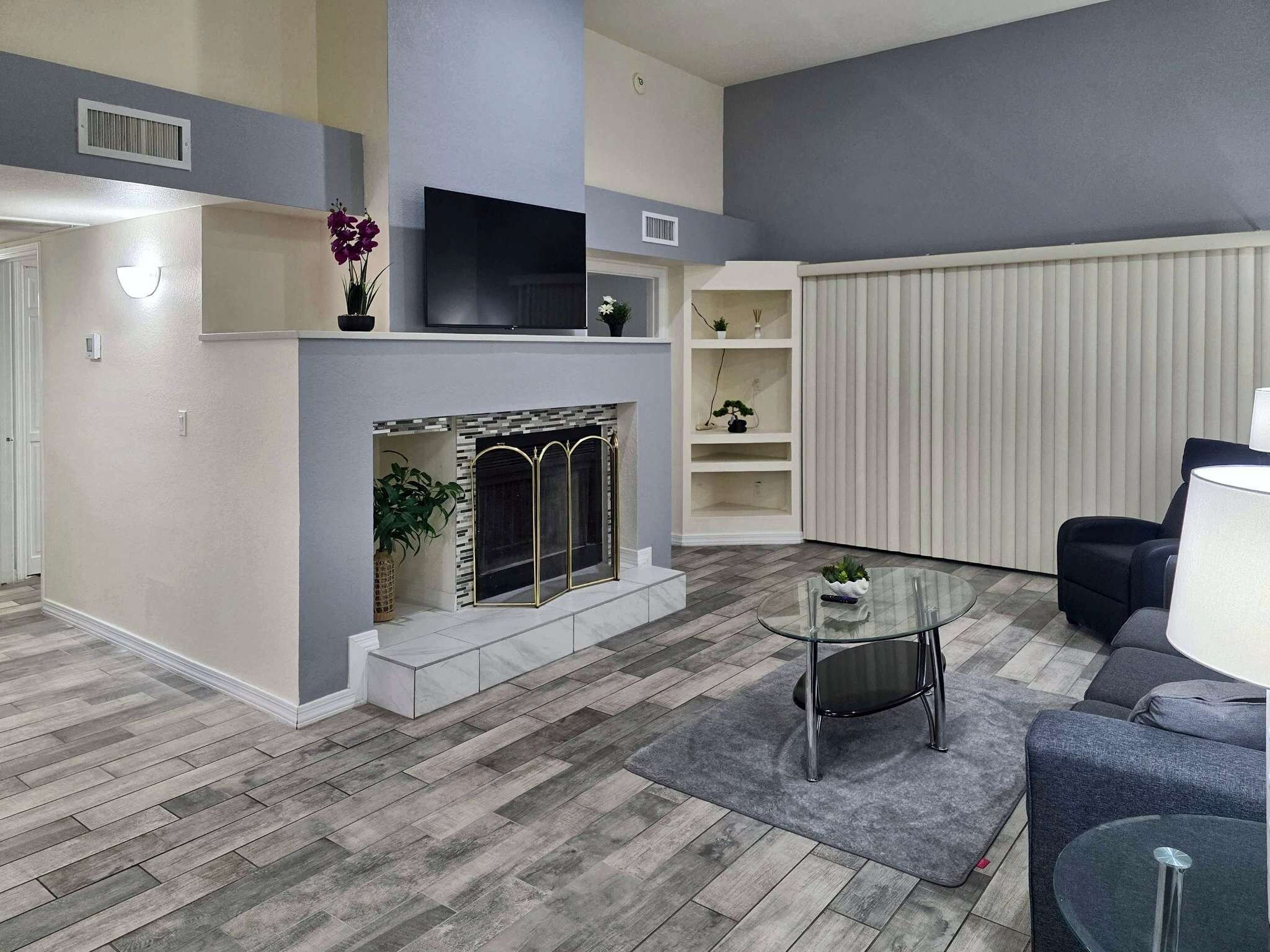 A modern living room with a fireplace, a flat-screen TV, and a glass coffee table.