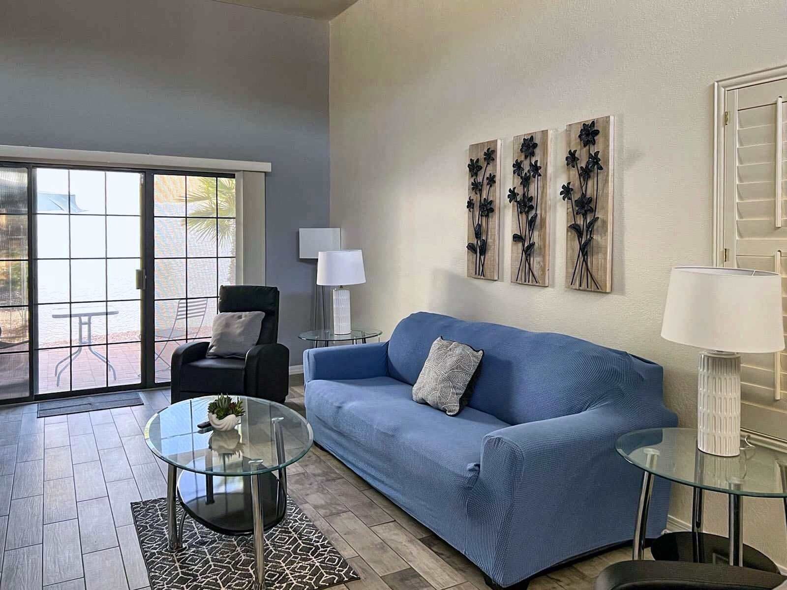 A living room with a blue sofa, a glass coffee table, a black armchair, and a patterned rug.
