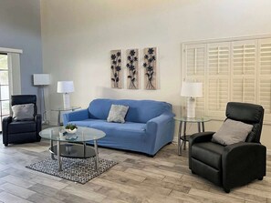 A living room with a blue sofa, two armchairs, a glass coffee table, and a patterned rug.