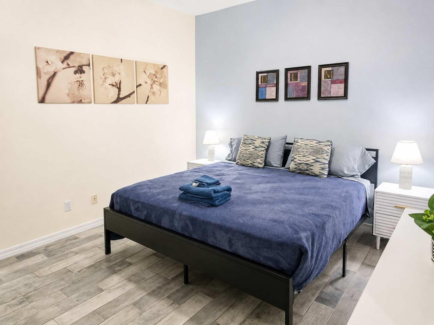 Une chambre à coucher avec un lit, des oreillers, une table de chevet et des œuvres d’art murales.