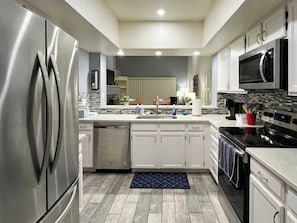 A modern kitchen with stainless steel appliances, white cabinetry, and a tiled backsplash.