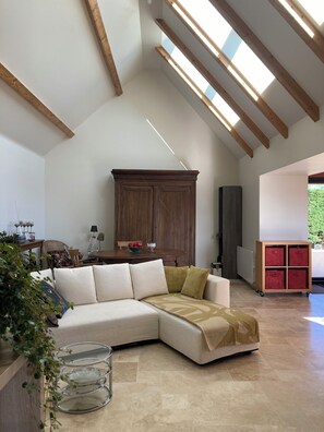 A spacious living area with a high ceiling, wooden beams, a sectional sofa, a cabinet, and a glass coffee table. - La Grange d'Ella in the Cotentin Peninsula, ocean view, beach 1 km away, near Barfleur (Vicq-sur-Mer)