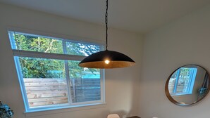 Ein Essbereich mit Holztisch, weißen Stühlen, einer hängenden Pendelleuchte, einem großen Fenster und einem Spiegel an der Wand.