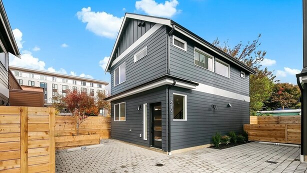 Ein modernes, zweistöckiges Haus mit dunkler Fassade, einer Haustür und einer kleinen Veranda.