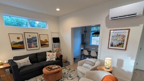 Ein modernes Wohnzimmer mit Sofa, Hocker und Sesseln, einem gemusterten Teppich und Kunstwerken an den Wänden.