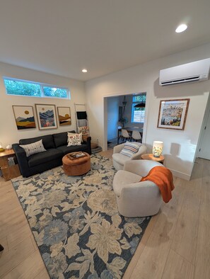 A modern living room with a sofa, ottoman, and armchair, a patterned rug, and artwork on the walls. - Live like a local in a brand-new pet-friendly home in the heart of Greenwood. (Seattle)