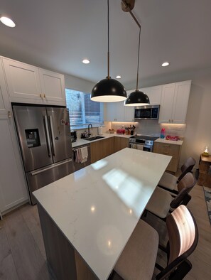 A modern kitchen with a central island, stainless steel appliances, and pendant lighting. - Live like a local in a brand-new pet-friendly home in the heart of Greenwood. (Seattle)