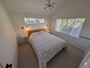 Een slaapkamer met een bed, twee bedlampjes, een raam met jaloezieën en een plafondlamp.