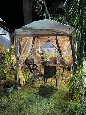 A tent with a table and chairs, surrounded by potted plants.