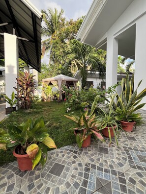 A covered outdoor area with potted plants, a grassy lawn, and a tiled floor.