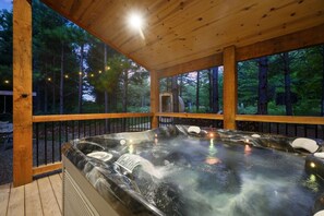 Ein Whirlpool mit Holzterrasse und Geländer, umgeben von Bäumen.