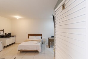 Quarto com cama, mesa de cabeceira e escrivaninha com cadeira.