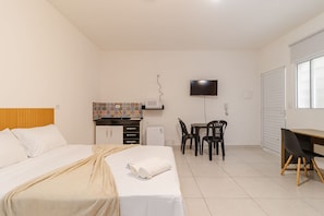 Quarto de hotel com cama, escrivaninha, cadeira, televisão e janela.