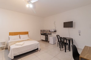 Quarto de hotel com cama, escrivaninha, cadeira, televisão, pequeno frigorífico e micro-ondas.
