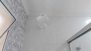 Een badkamer met een betegelde muur, een douche met een witte douchekop en een glazen douchecabine.