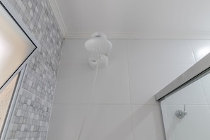 Un baño con pared de azulejos, ducha con cabezal blanco y mampara de vidrio.