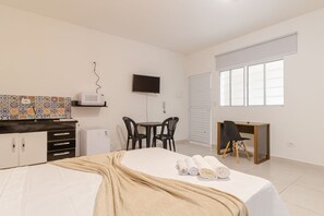 Habitación de hotel con cama, escritorio, televisión, ventana y kitchenette.