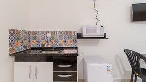 Een kleine keuken met een magnetron, een kleine koelkast en een betegelde spatwand.
