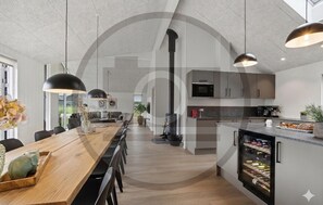 A modern kitchen with a built-in wine cooler, a dining area with a long wooden table, and pendant lighting. - Gorgeous home in Rødby with sauna (Rødby)