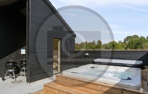 A modern outdoor hot tub area with a wooden deck, a grill, and a door leading to a covered space. - Gorgeous home in Rødby with sauna (Rødby)