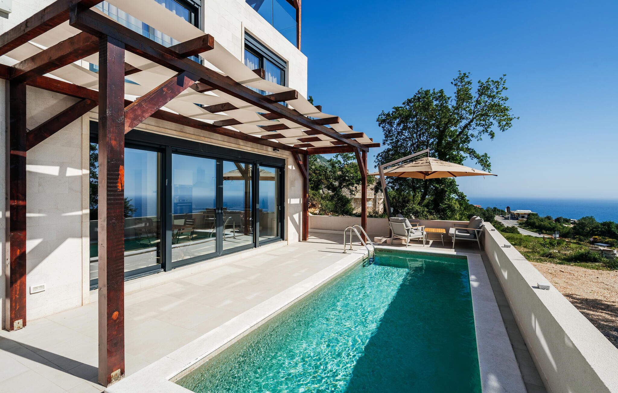 Un espace piscine extérieur moderne, agrémenté d’une pergola, de chaises longues et offrant une vue sur la mer.