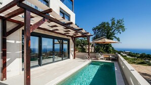 Un espace piscine extérieur moderne, agrémenté d’une pergola, de chaises longues et offrant une vue sur la mer.