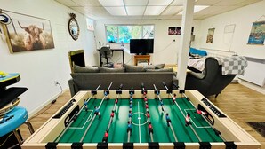 A room with a foosball table, a sofa, a bed, and a television. - Welcome to the Tree House apartment- a family friendly retreat with arcade games (Lake Forest Park)