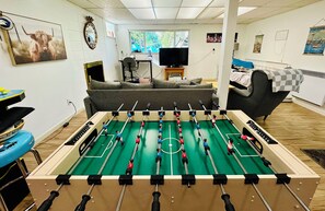 Een kamer met een tafelvoetbaltafel, een bank, een bed en een televisie.