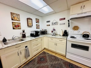 A kitchen with white cabinets, a granite countertop, a microwave, a kettle, and various wall decorations.
